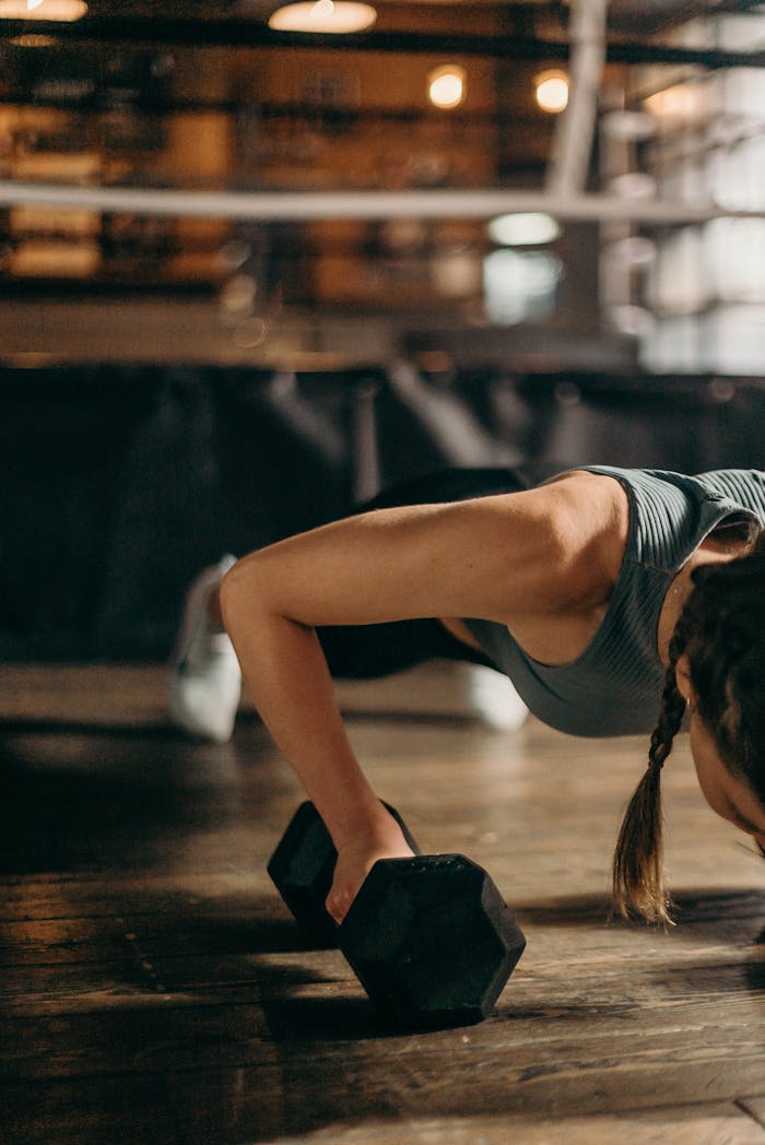 pexels-photo-4753996-1 Fit woman doing a dumbbell push-up in a gym, highlighting strength and fitness training.